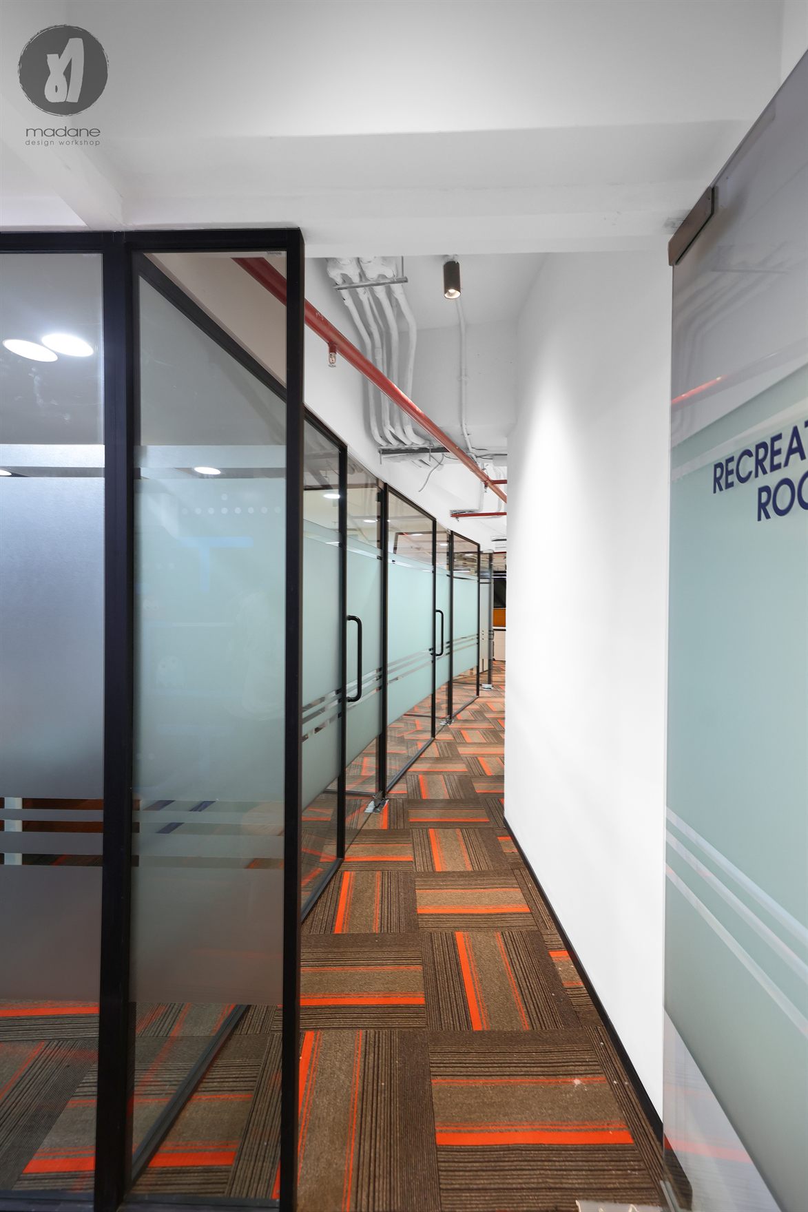 Corridor lined with frosted glass partitions and orange-striped carpet tiles leading past a Recreation Room graphic wall