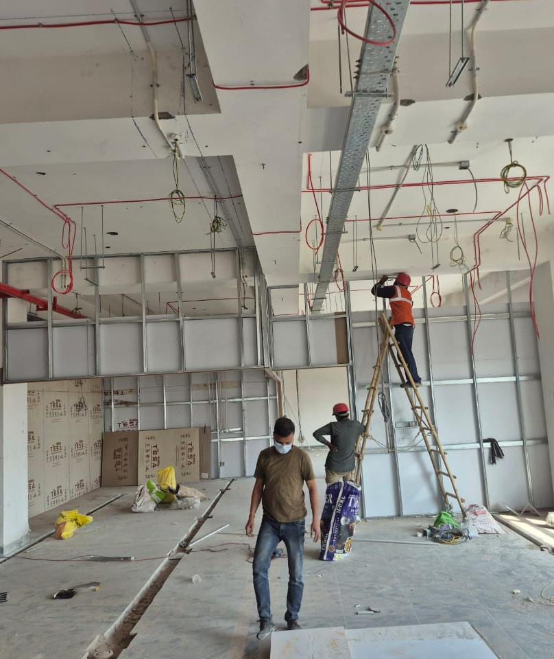 Office floor under construction with exposed-services ceiling, scaffolding and workers.
