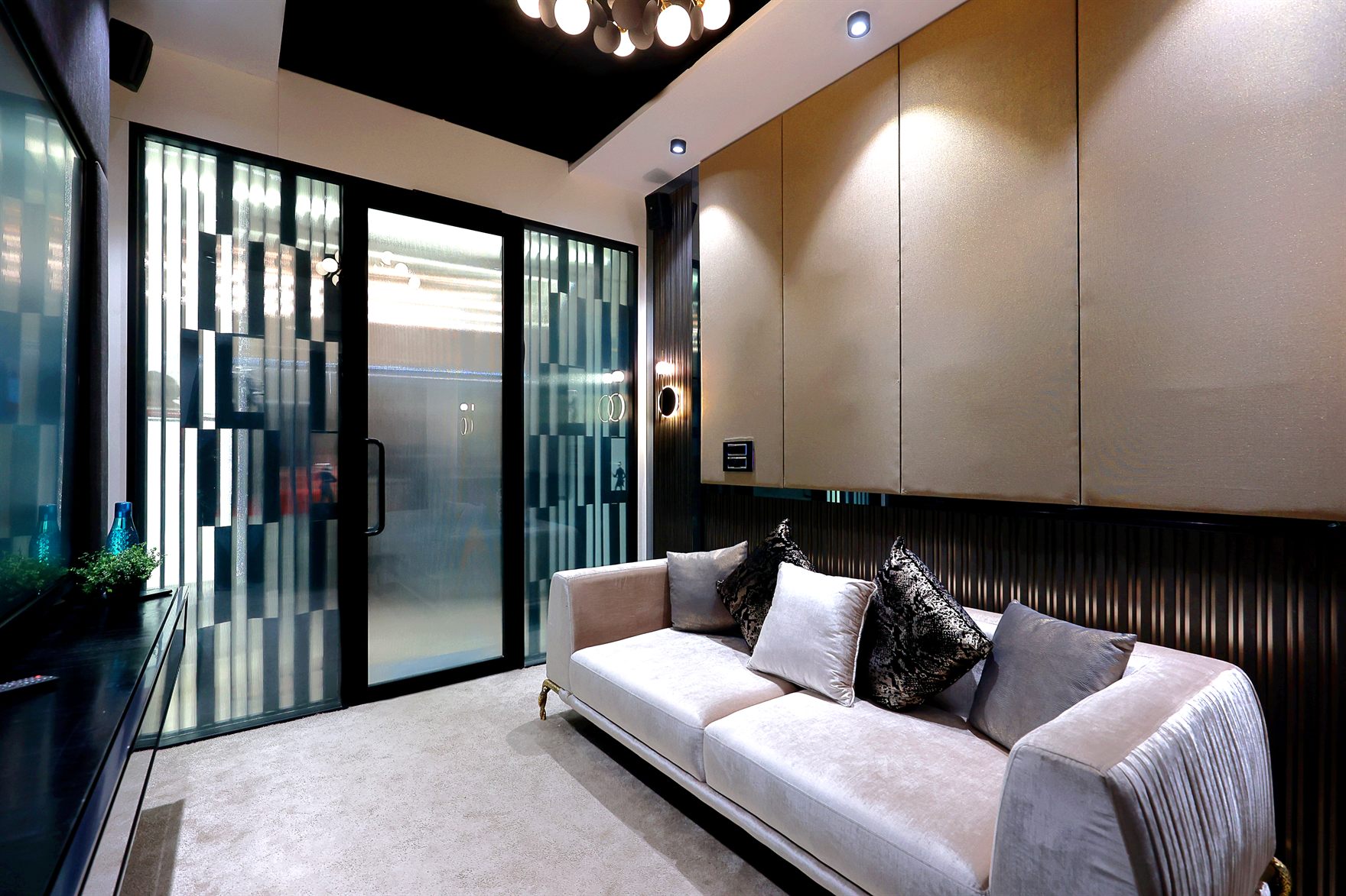 Client lounge with a beige velvet sofa and patterned cushions against gold upholstered wall panels and a fluted black dado, framed by striped glass sliding doors