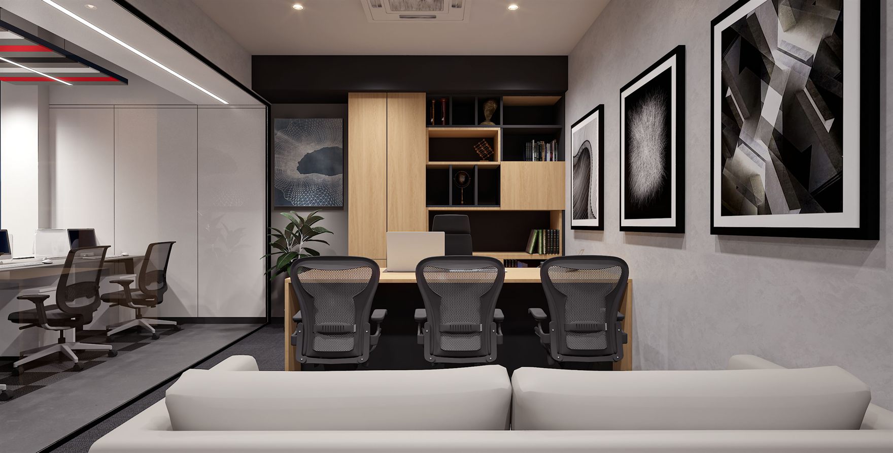 Director cabin with an oak desk and black mesh chairs, tall oak storage joinery, framed monochrome artworks on a grey wall and a white sofa, beside a glazed workstation area