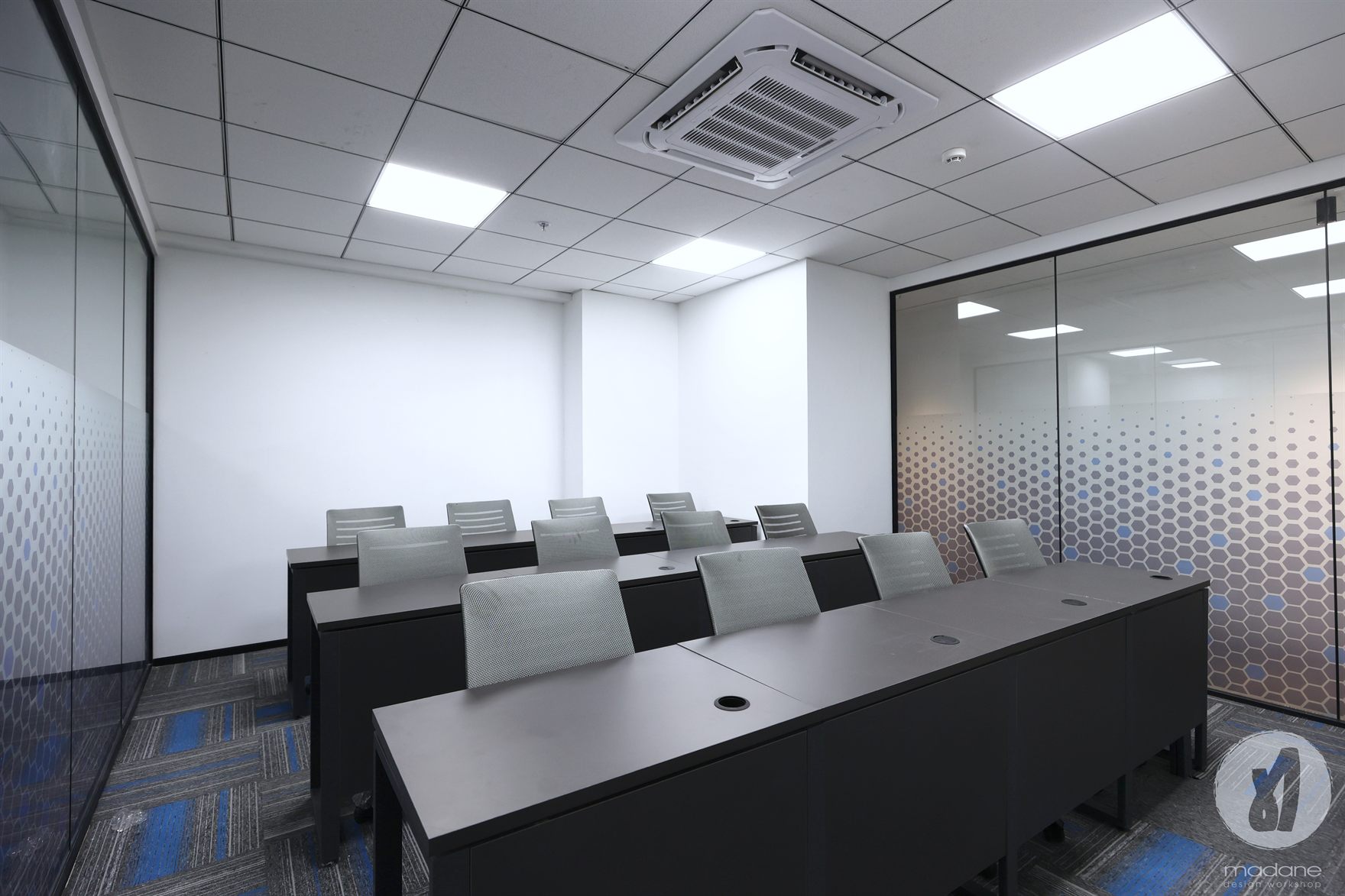 Meeting room with dark tables and grey chairs between glass walls carrying graded blue honeycomb frost film